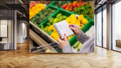 Woman with notebook in grocery store, closeup. Shopping list on paper. Wall mural