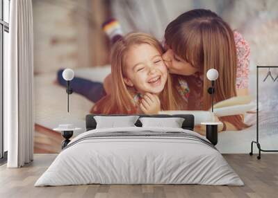 Portrait of a smiling young cute mother and daughter reading a book lying and relax in the bed in a bright big white room  Wall mural