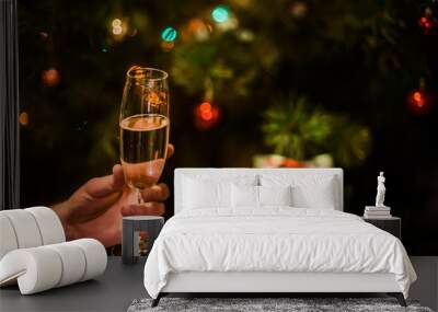 Glass with champagne in hand on a Christmas tree background Wall mural