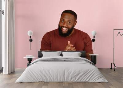 Smiling Afro-American man trickster rubs hands ready for cozy deal standing on light pink background in studio close view Wall mural