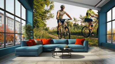 A man and a woman ride bicycles on a dirt road in the summer at sunset. Active rest in the summer on bicycles. Wall mural