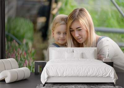 A woman with a small daughter make a selfie in a greenhouse with flowers. Wall mural