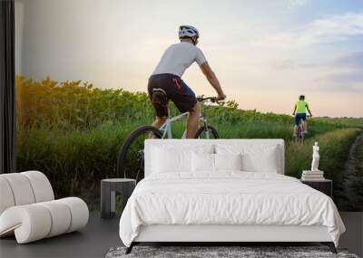 young man and woman ride bicycles between fields in summer. Wall mural