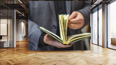 A man in a dark business suit flips through the pages of a book. Book in a green cover. Selective focus. Wall mural