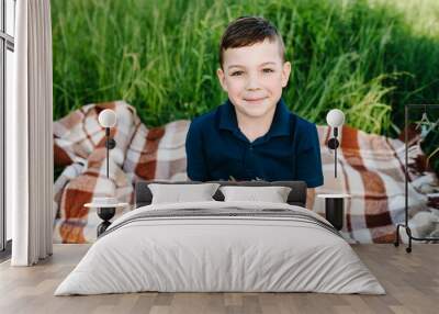 A plate of strawberries in the hands of a guy. Portrait of boy eating strawberries on grass, nature. Happy on vacation outdoors. The little son having picnic on blanket. The concept of family holiday. Wall mural