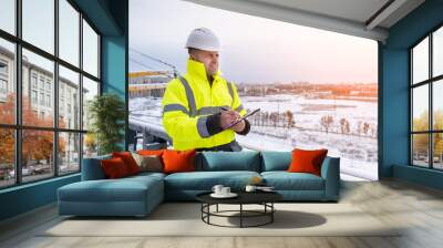 a smiling caucasian builder in a white hard hat and yellow fluorescent jacket holds clipboard Wall mural