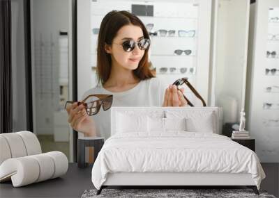 A young woman chooses on sunglasses in an optics store Wall mural