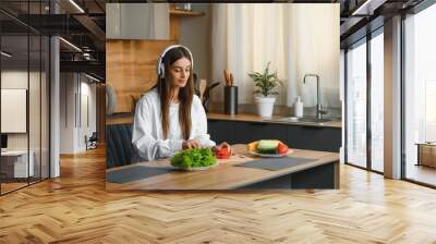 Adorable nice charming cheerful pretty beautiful stylish excited girl listening to music, singing in modern light white kitchen, cooking homemade dish with domestic products Wall mural