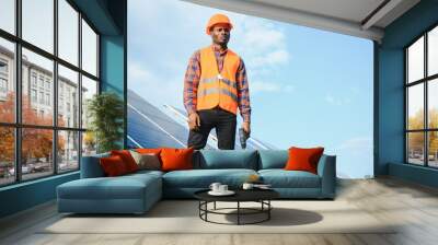 African american man in safety helmet on solar panels with screwdriver. Competent technician using tools while performing service work on station Wall mural