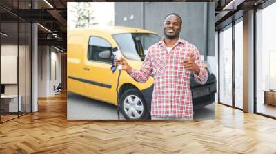 African american Man stands next to electric delivery vans at electric vehicle charging station Wall mural