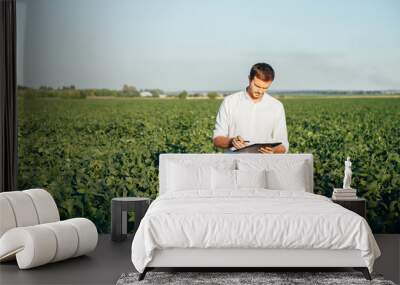 Agronomist holds tablet touch pad computer in the soy field and examining crops before harvesting. Agribusiness concept. agricultural engineer standing in a soy field with a tablet in summer. Wall mural