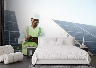 An African-American engineer in a white shirt and hard hat is working on a field of solar panels. Solar renewable energy concept. Wall mural