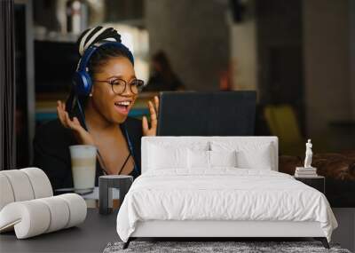 Attractive African American blogger with headphones and laptop communicating with followers in cafe Wall mural