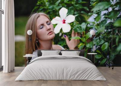 Beautiful, young, slender, long-haired blond girl in white  dress on background of flowers, nature. Turkey. Model stylish. Fashion. Woman with eyes closed. stylish makeover. Close up hibiscus flower Wall mural