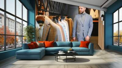 Businessman in classic vest against row of suits in shop Wall mural