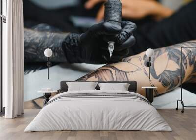 Cropped close up of a bearded tattoo artist working at his studio tattooing sleeve on the arm of his male client. Man getting tattooed by professional tattooist Wall mural