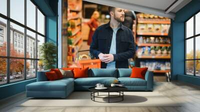 Customer In Supermarket. Man Doing Grocery Shopping Standing With Cart Choosing Food Product Indoors. Guy Buying Groceries In Food Store. Selective Focus, Copy Space. Wall mural