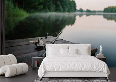 Fishing rod, spinning reel on the background pier river bank. Sunrise. Fog against the backdrop of lake. Misty morning. wild nature. The concept of rural getaway. Article about fishing day. Wall mural