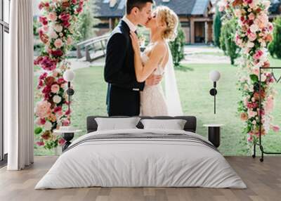 Happy bride and groom kissing after wedding ceremony. couple newlyweds.Wedding ceremony under the arch decorated with flowers and greenery. Wall mural