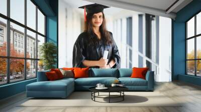 Happy Indian university student in graduation gown and cap holding diploma certificate. Wall mural