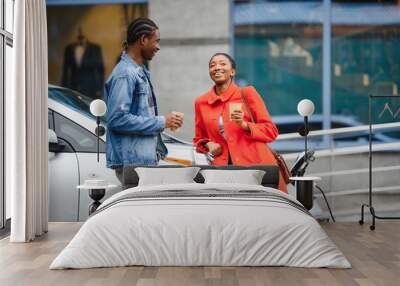 Happy young adult african american man and smiling woman charging electric car. Wall mural