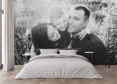 Happy young family spending time together outside in nature on vacation outdoors. Mom, dad and son sit in the grass. The concept of family holiday. Black and white photo. Wall mural