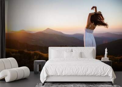 Hiker woman standing with hands up achieving the top. Girl welcomes a sun. Conceptual design. Successful woman hiker open arms on sunrise mountain top. Girl in long white dress in the mountains. Wall mural