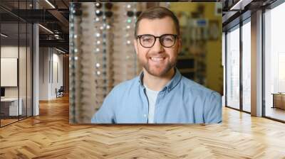 In Optics Shop. Portrait of male client holding and wearing different spectacles, choosing and trying on new glasses at optical store. Man picking frame for vision correction, closeup Wall mural