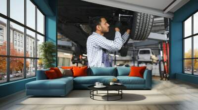 latin hispanic auto mechanic in uniform is examining a car while working in auto service Wall mural