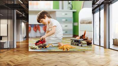 Little boy playing toy cars on play mat. Young kid with colorful educational vehicle and transport toys on carpet. City street map rug. Child driving car to parking garage. Kids at home or daycare. Wall mural