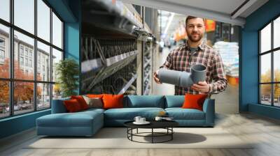 male plumber in a hardware store chooses the sewer pipes, the concept of plumbing work in the house Wall mural