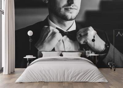 Man in a suit correcting his bow-tie. Morning preparation groom at home. Fashion photo of a man. Black and white photo. Wall mural