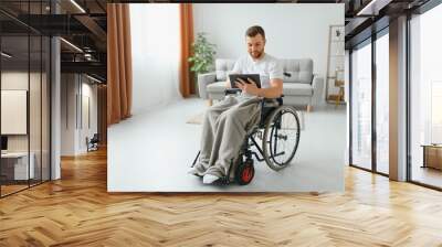 Man in wheelchair using tablet computer at home. Positive retired male with physical disability browsing web on touch pad, watching video online indoors Wall mural