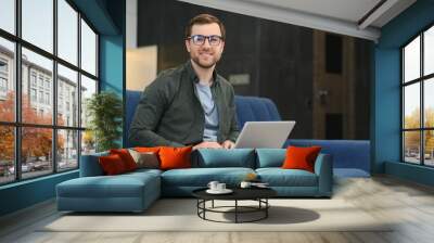 Men working on laptop computer in his room. Home work or study, freelance concept. Young man sitting relaxed on sofa with laptop. Modern businessman using laptop. Wall mural