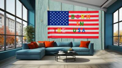 On the flag of the USA, the text BORN IN THE USA is lined with multicolored letters on a wooden background. Wall mural