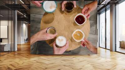 People drinking coffee and tea high angle view. Many female hands hold cups with hot various drinks. Cups with tea, coffee, cappuccino, and latte stand on a round wooden table. Top view. Closeup. Wall mural