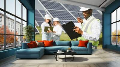 Portrait of engineers standing outside near solar panels. Three workers, two woman and one men Wall mural