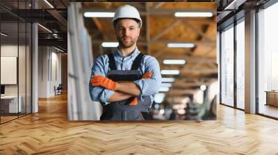 Portrait of factory worker in protective uniform and hardhat standing by industrial machine at production line. People working in industry Wall mural