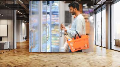 Portrait of handsome young Indian man standing at grocery shop or supermarket, Closeup. Selective Focus. Wall mural