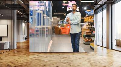 Portrait of handsome young Indian man standing at grocery shop or supermarket, Closeup. Selective Focus. Wall mural