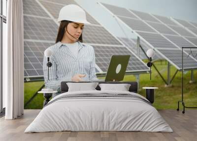 Portrait of young female engineer standing near solar panels. Beautiful female professional in white helmet Wall mural