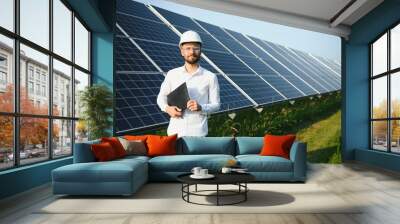 Positive bearded male investor standing against photovoltaic panels producing alternative energy. Wall mural