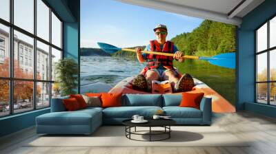 the guy is sailing on a red kayak, wearing a life jacket with glasses and a cap. Holds a paddle in his hand Wall mural