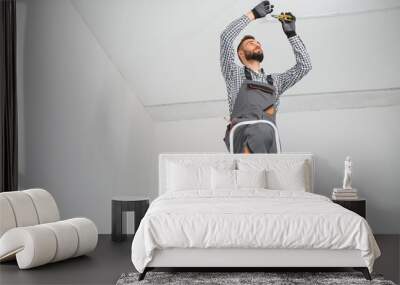 Repairman or professional electrician in workwear installing light spots, standing on the ladder in the white living room Wall mural