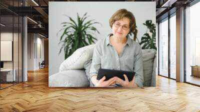 Senior woman looking and laughing at her digital tablet on sofa Wall mural