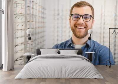 Shot of a handsome bearded man trying on new glasses at the eyewear store.Man buying glasses.Health, eyesight, vision, fashion, shopping Wall mural