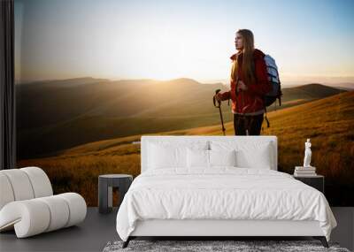 Shot of a young woman looking at the landscape while hiking in the mountains. Happy traveler with backpack standing on top of a mountain and enjoying sunset view Wall mural