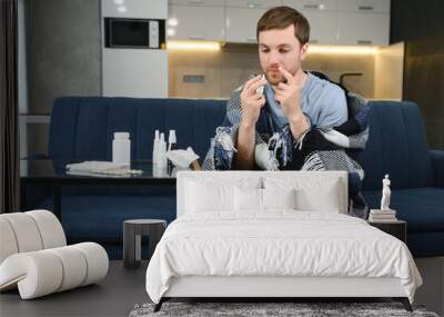 Sick man on sofa at home in living room. man feeling sick with cold and fever at home, ill with flu disease sitting on the sofa. It's the season of sneezes. Wall mural