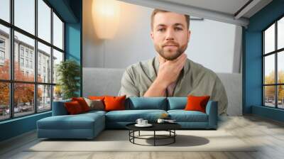 Sore throat. Dark-haired young man having a sore throat. Wall mural