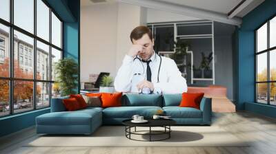 Stressed male doctor. Mid adult male doctor working long hours. Overworked doctor in his office. Not even doctors are exempt from burnout . Wall mural